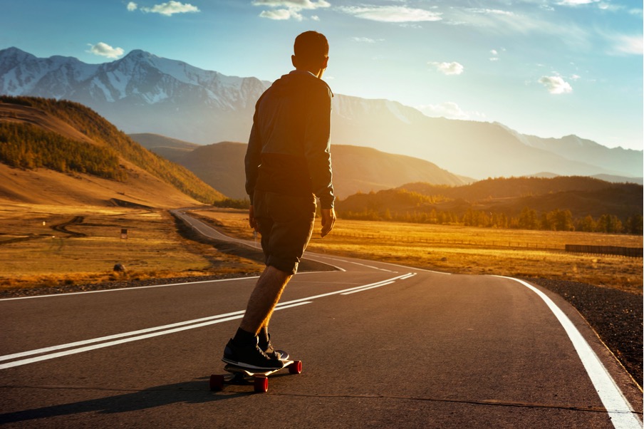 A man rides on the straight road on a longboard at sunset time